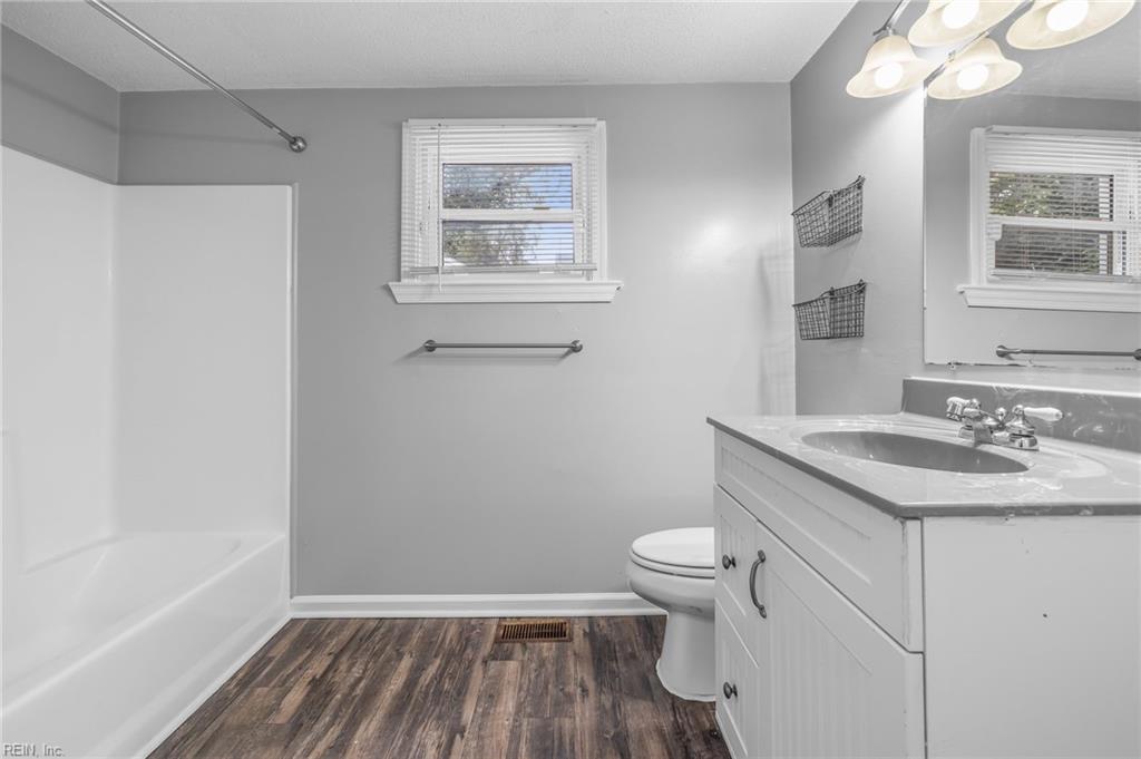 Bathroom with a white tub, vanity, two windows, and dark wood-look flooring.