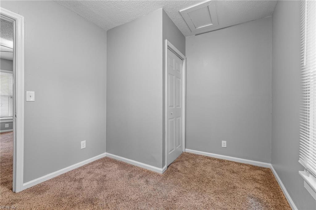 Empty bedroom with beige carpet, a white closet door, and a window with blinds.