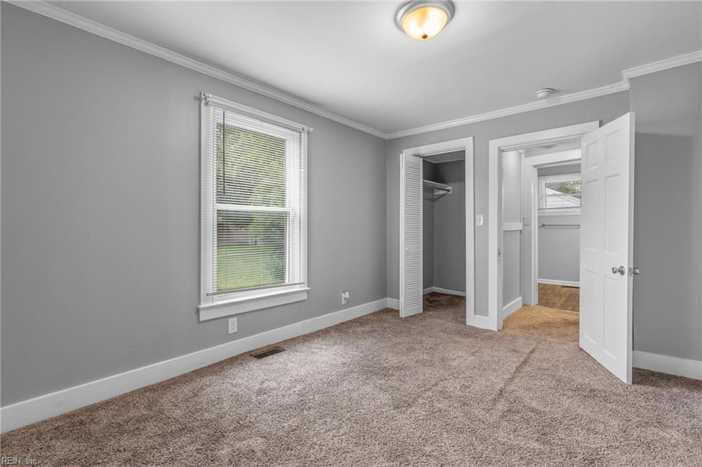 Empty bedroom with gray walls, beige carpet, a window with blinds, and an open closet.