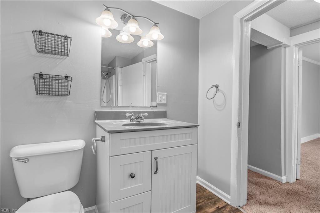 Bathroom with white vanity, sink and mirror beside a toilet, opening to a carpeted hallway.