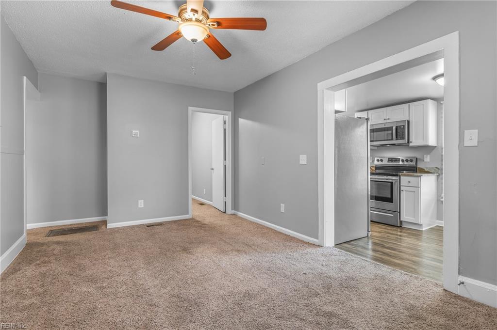 Unfurnished living room with beige carpet, a ceiling fan, and an adjoining kitchen.