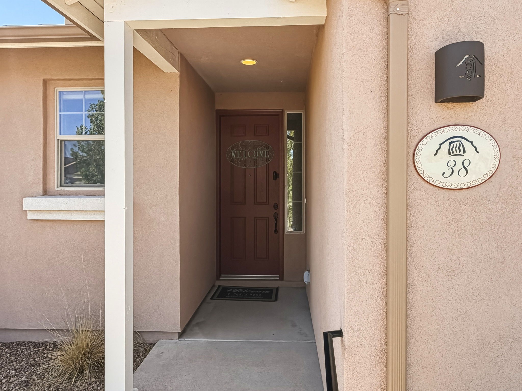 Covered entry with a dark wood front door and oval address plaque marked 38.
