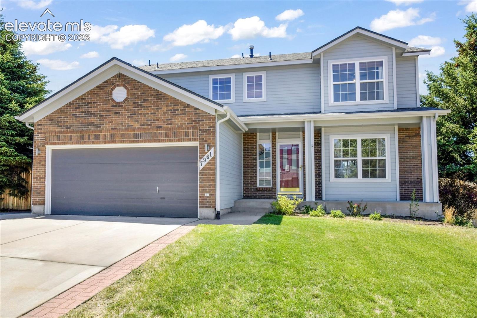 Two-story gray-and-brick home with a two-car garage, covered entry, and front lawn.