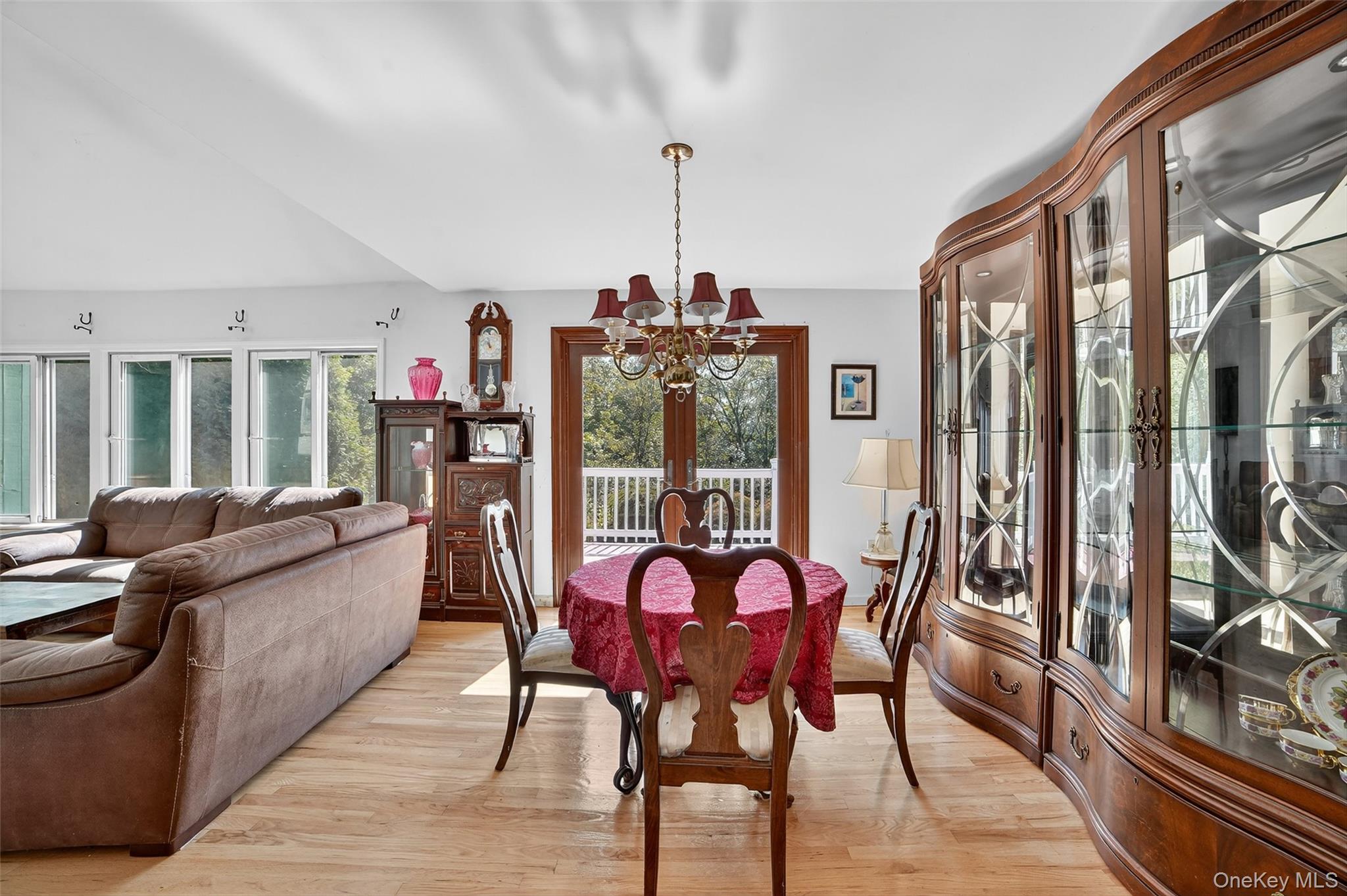 Furnished dining and living area with a red-covered table, curved china cabinet, and deck access.