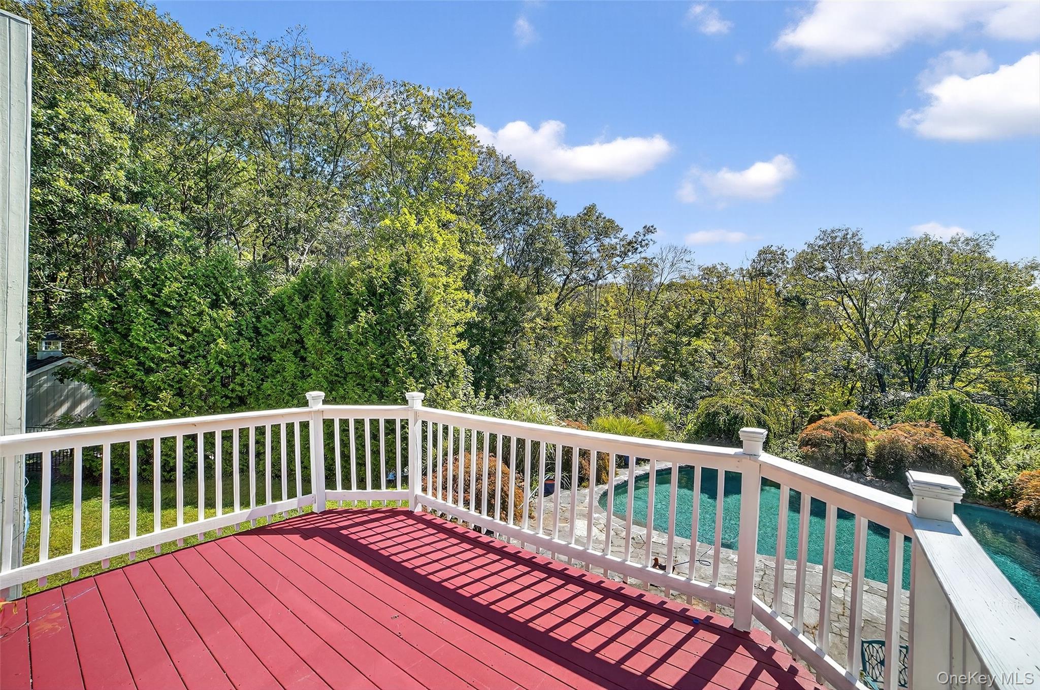 Red deck overlooks a swimming pool and wooded yard.