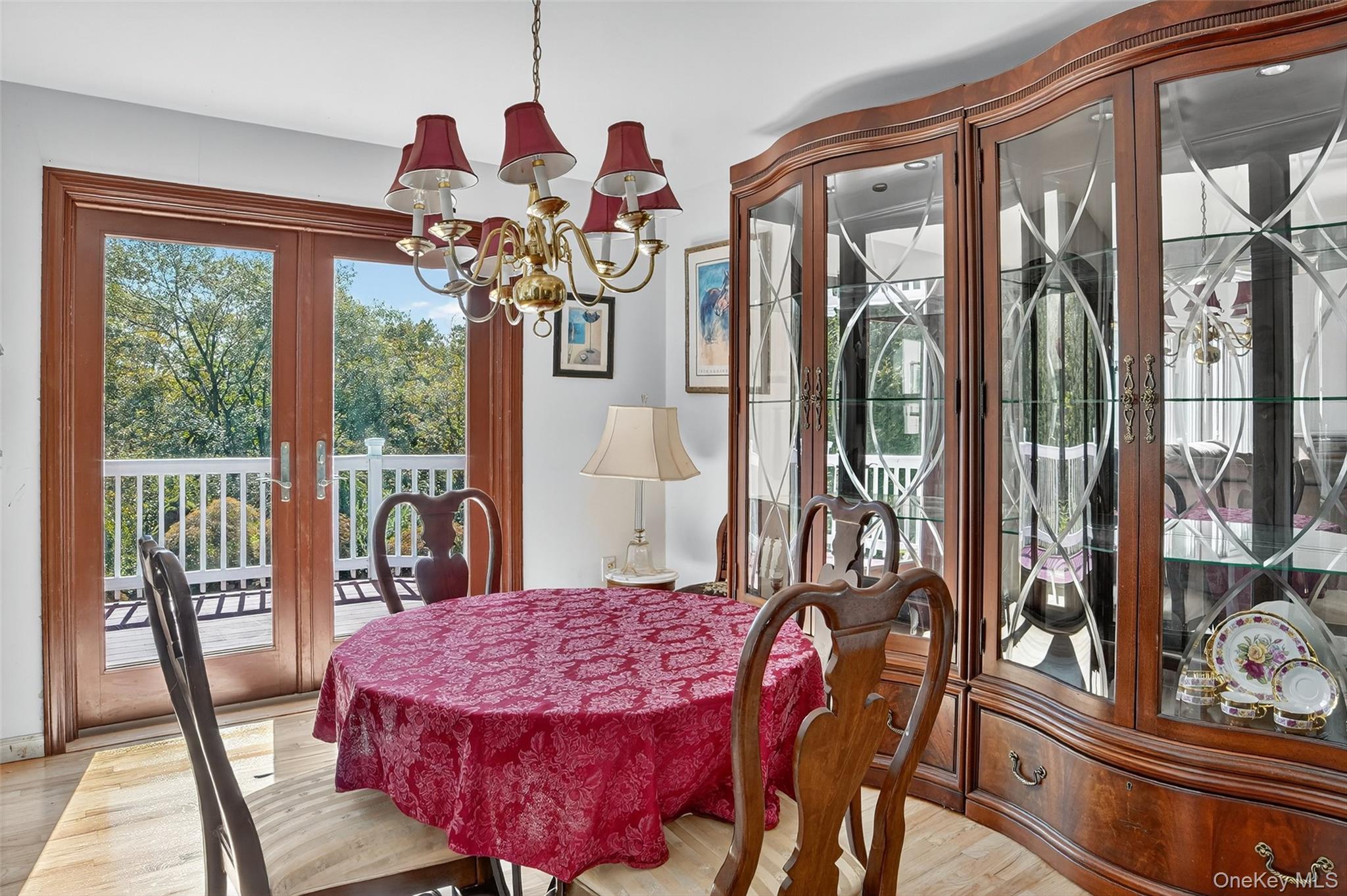 Dining room with a red-covered table, china cabinet, and French doors opening to a deck.