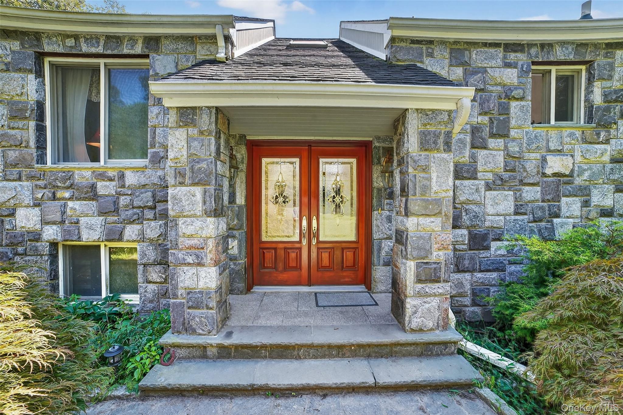 Stone home entrance with decorative-glass double doors beneath a covered porch.