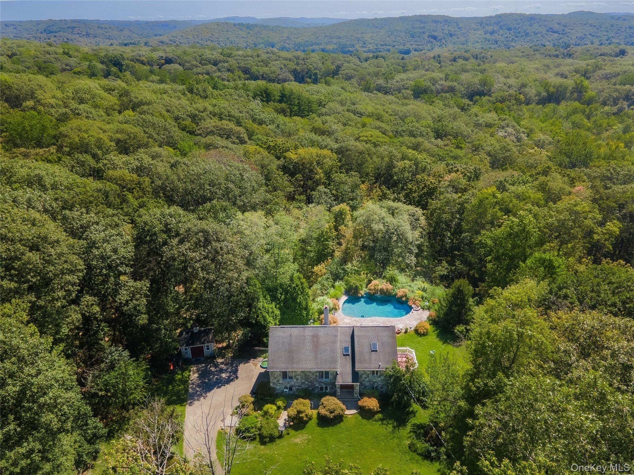 Aerial view of a stone house and swimming pool surrounded by woodland and forested hills.