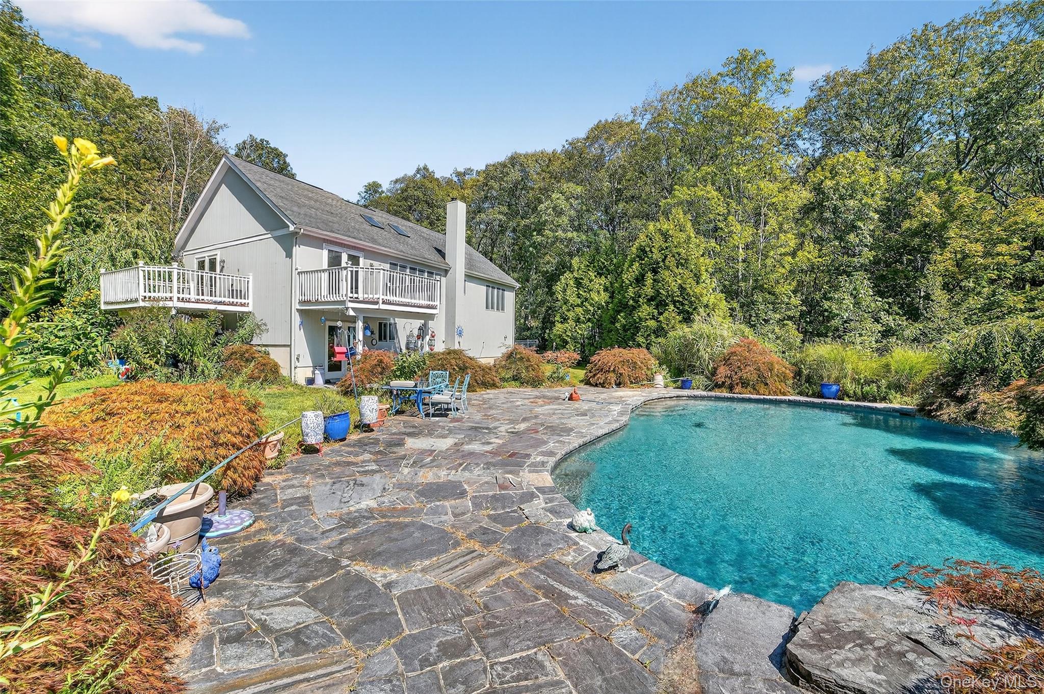 House with elevated decks overlooking a curved swimming pool and stone patio.