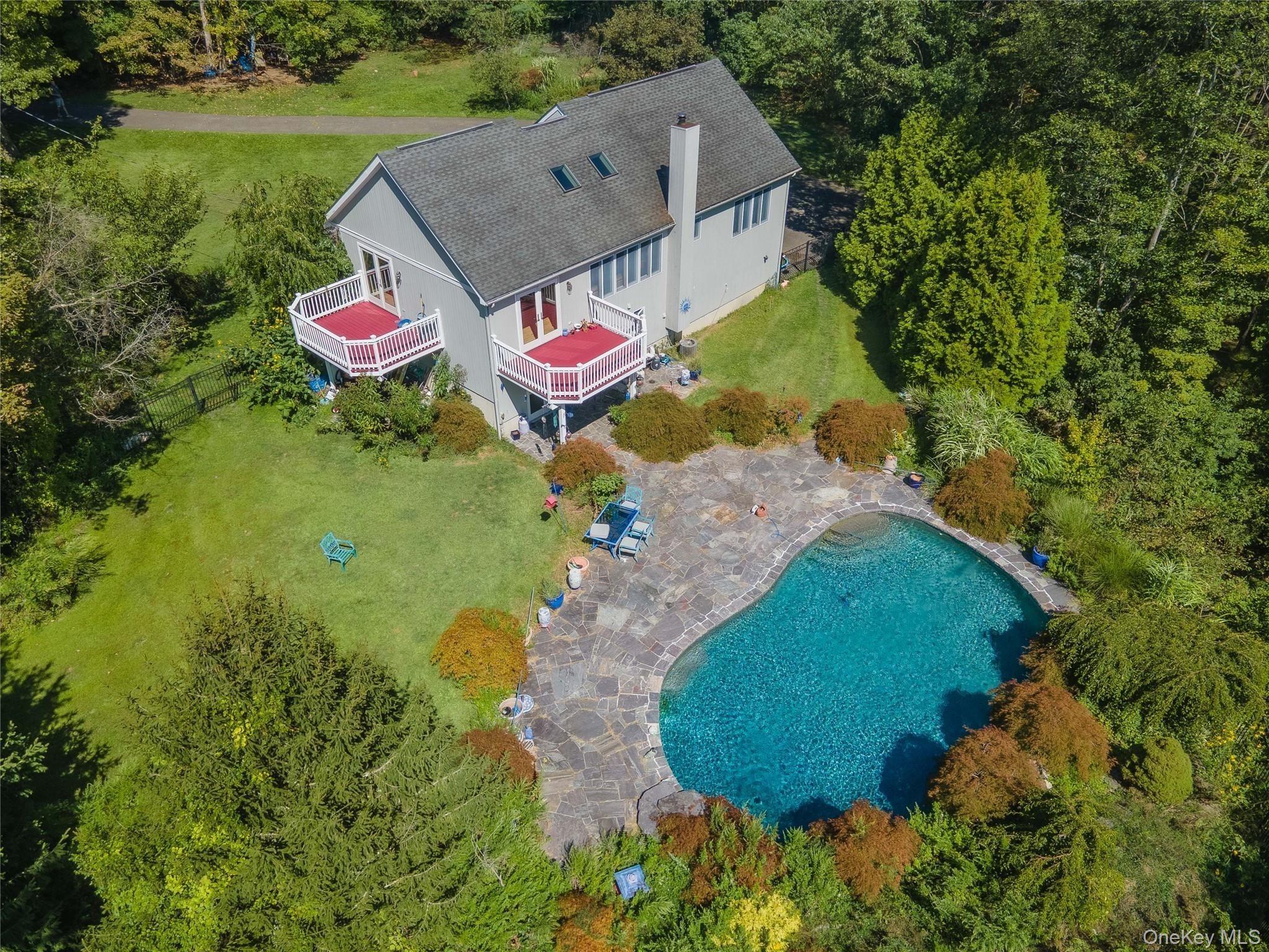 Aerial view of a house with red decks, a curved pool, and a stone patio.