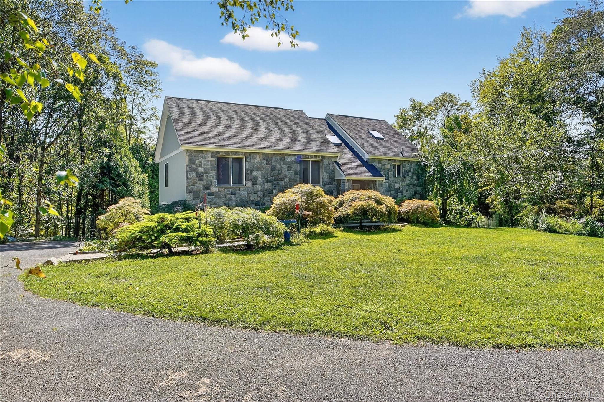 Stone-faced house with steep roof, landscaping, mature trees, and a broad front lawn.
