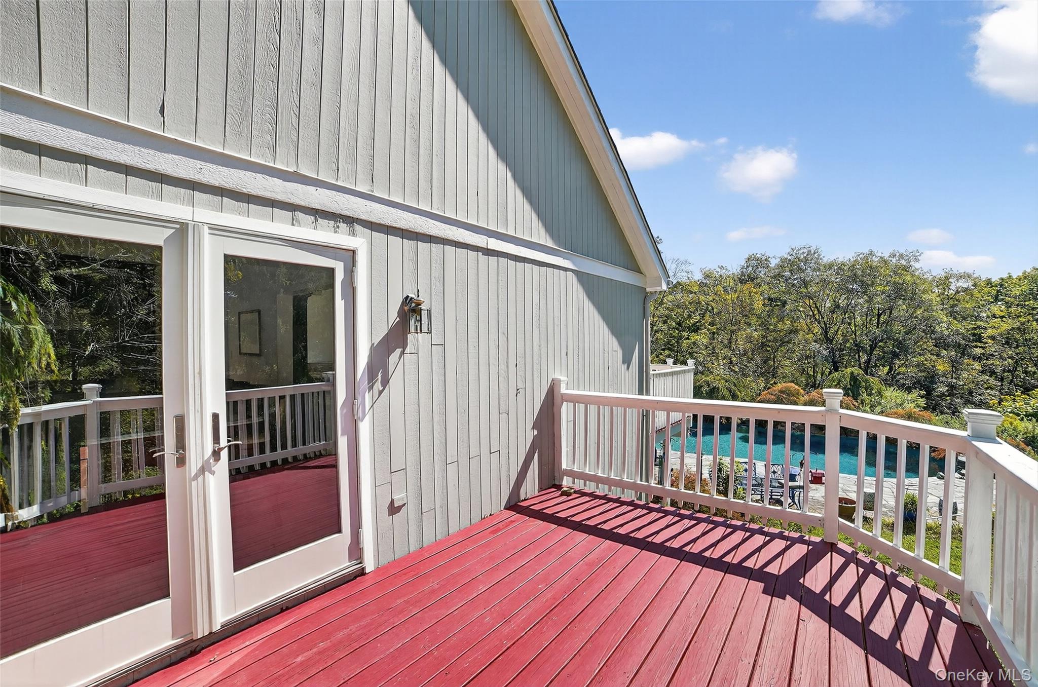 Red wooden deck with white railings overlooking a swimming pool and wooded yard.