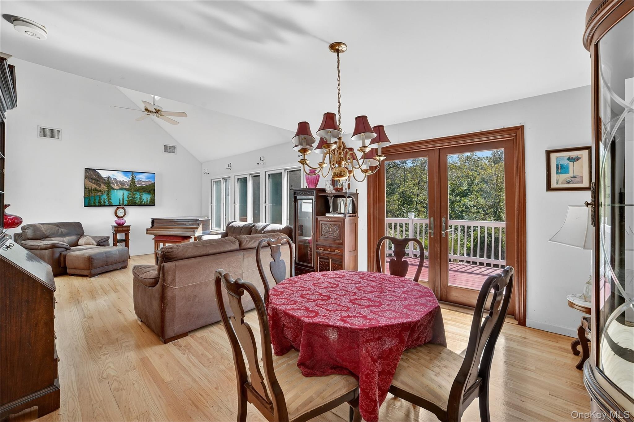 Dining and living room with a red-covered table, chandelier, and sliding doors to a wooded deck.
