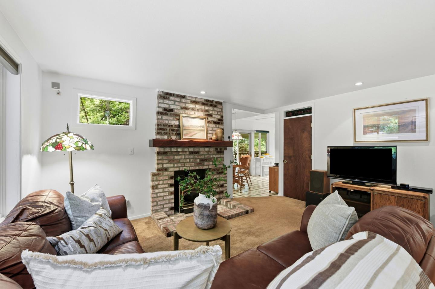 Living room with a brick fireplace, brown leather sofas, and a view into the dining area.