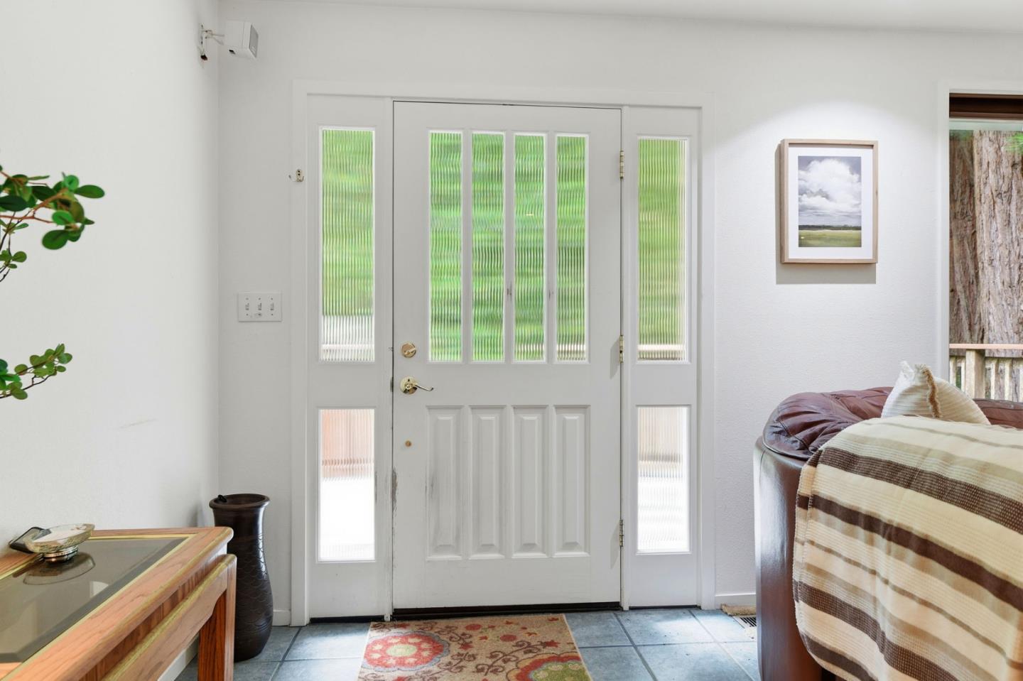 Home entryway with a white glass-paneled front door, tiled floor, patterned rug, and leather sofa.