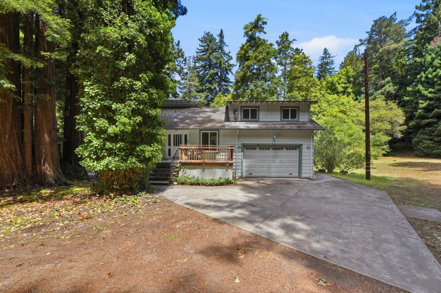 Two-story house with an attached garage and wooden porch, surrounded by tall redwoods.