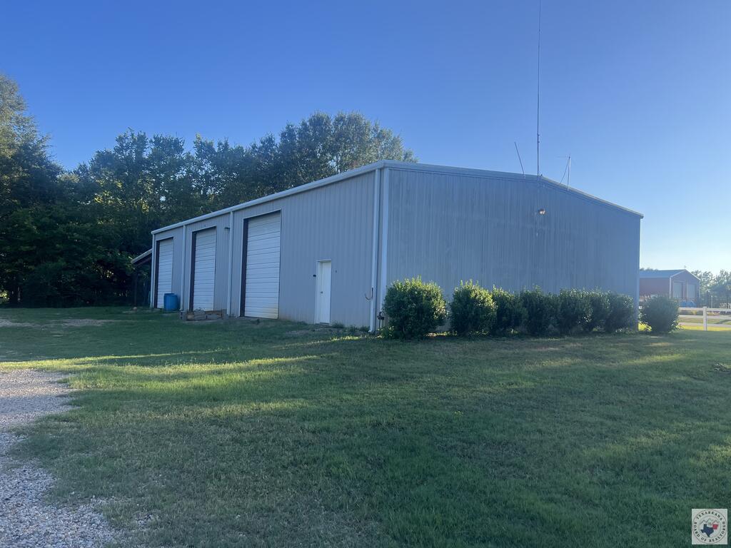 Metal workshop with three roll-up doors beside a grassy lawn and gravel drive.