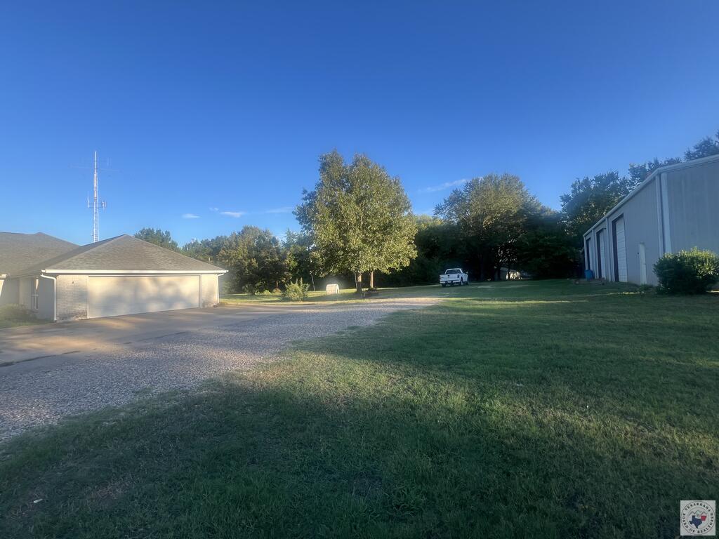 House with attached garage, gravel drive, broad lawn, and large metal outbuilding.