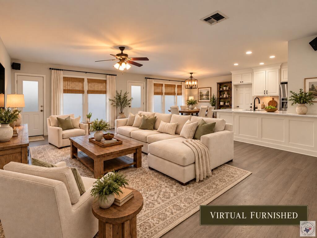Open-plan living room with a cream sectional, wood coffee table, and adjoining white kitchen.