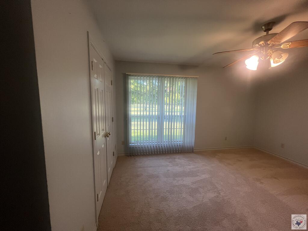 Vacant bedroom with beige carpet, closet doors, and a large window with vertical blinds.