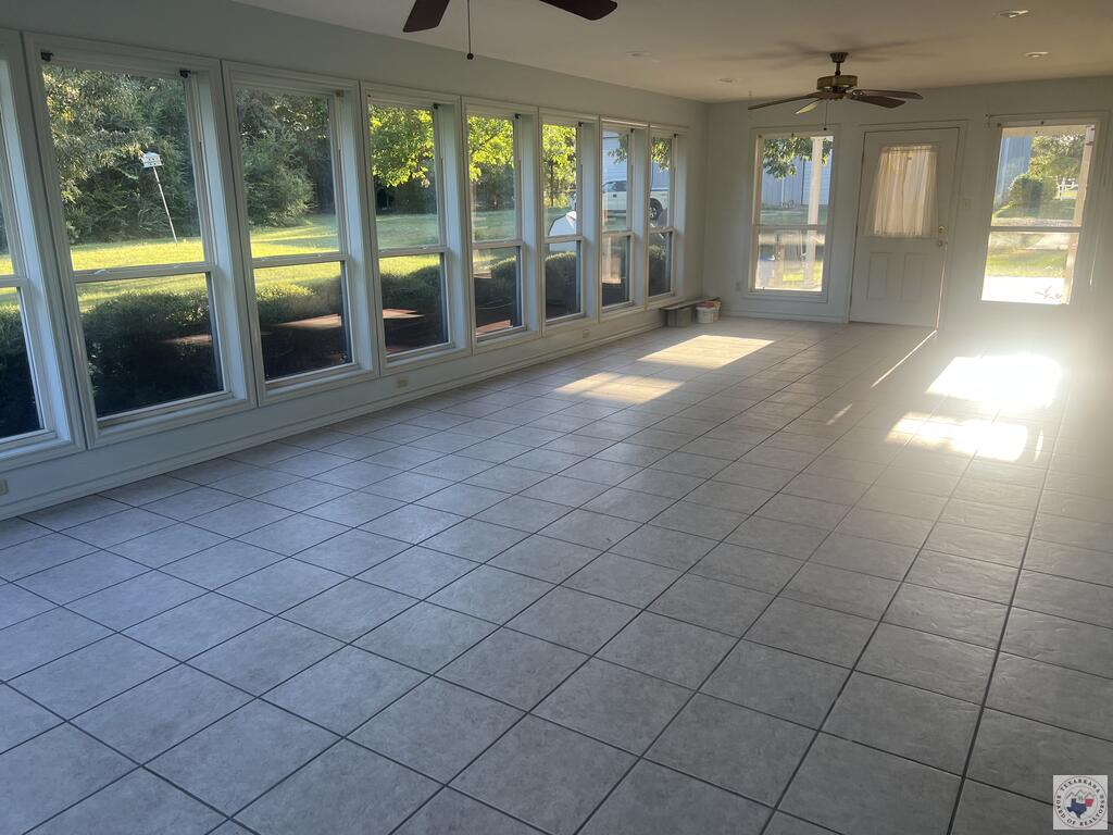 Empty sunroom with expansive windows, gray tile flooring, and sunlight across the floor.