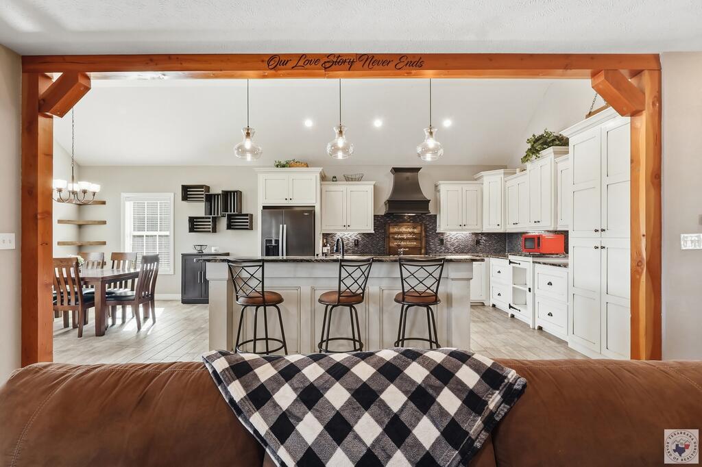 Open-plan kitchen with a large white island, three stools, and a dining table framed by a rustic wooden beam.