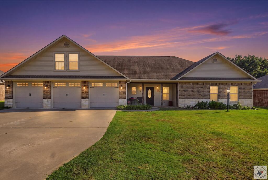 Single-story brick-and-siding home with three garage doors and a broad driveway at dusk.