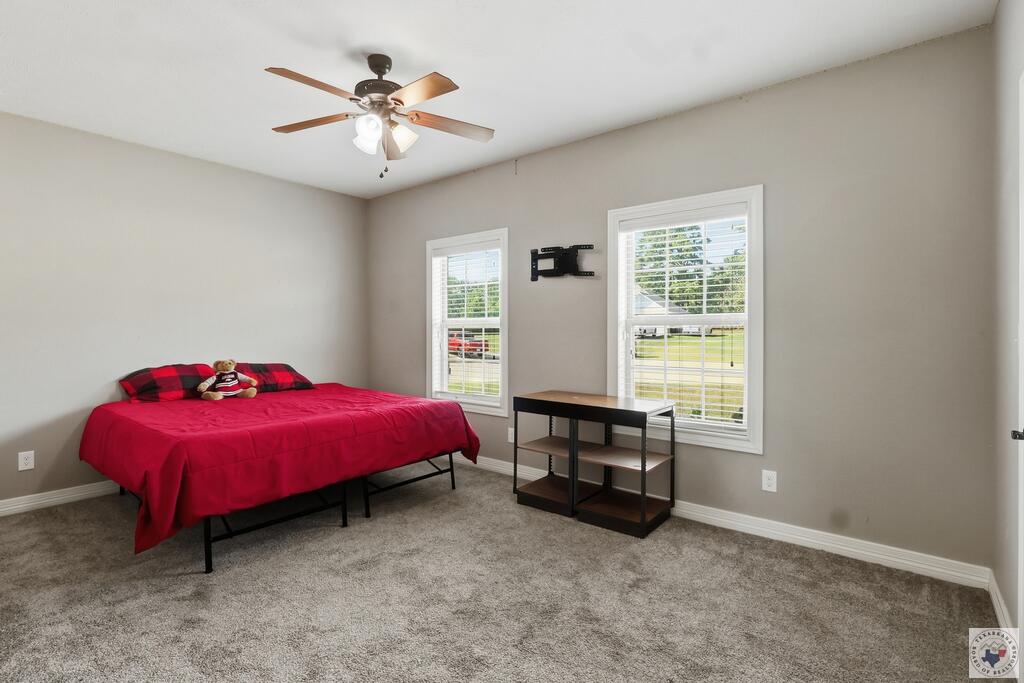 Bedroom with a bright red bed, two windows with white blinds, and a ceiling fan.