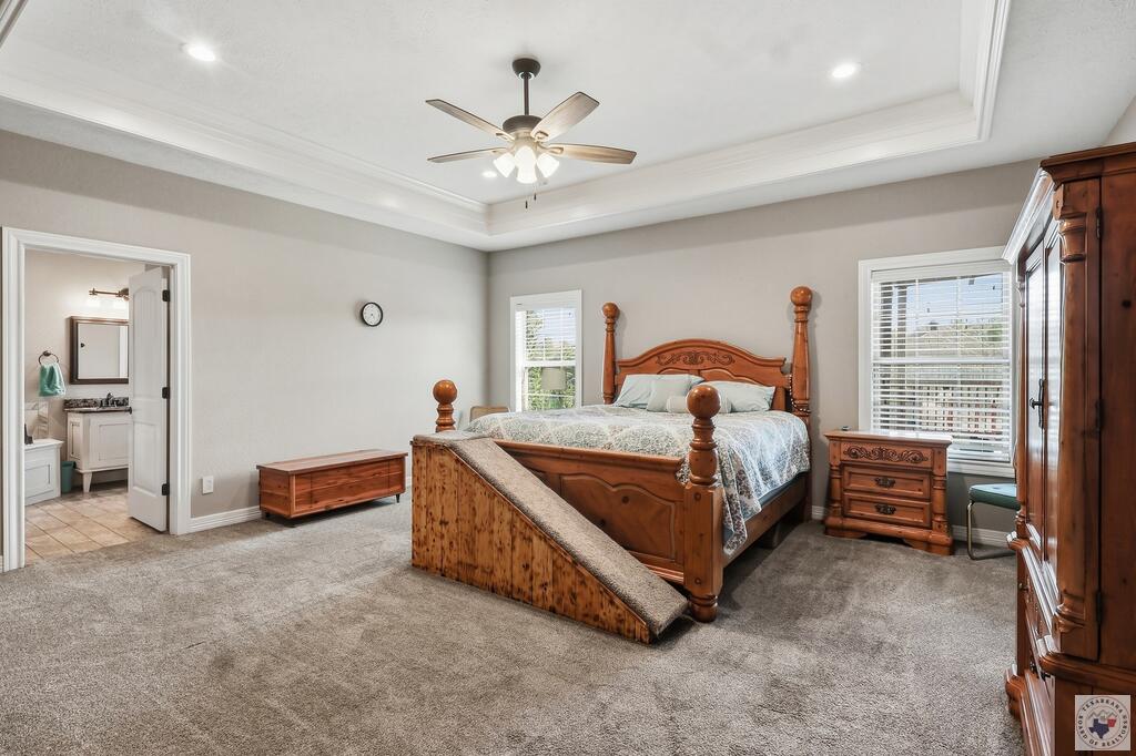 Bedroom with carved wooden bed, tray ceiling, carpet, and doorway to an adjoining bathroom.