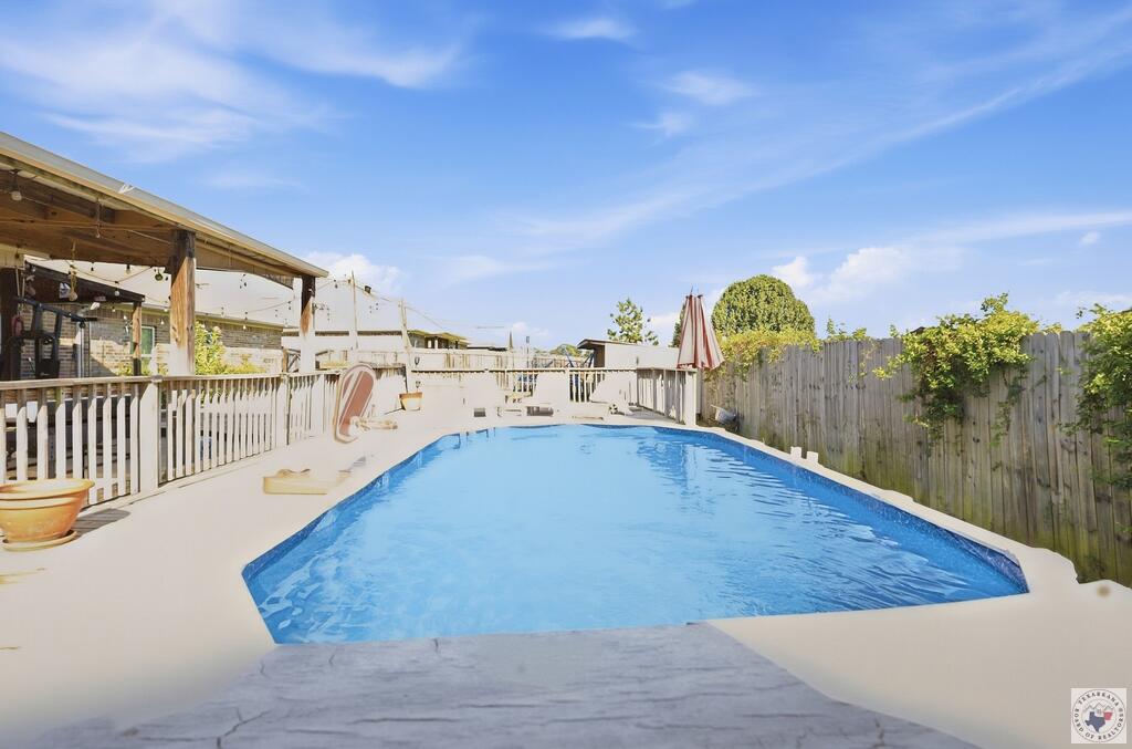 Backyard swimming pool beside a covered patio and tall wooden privacy fence.