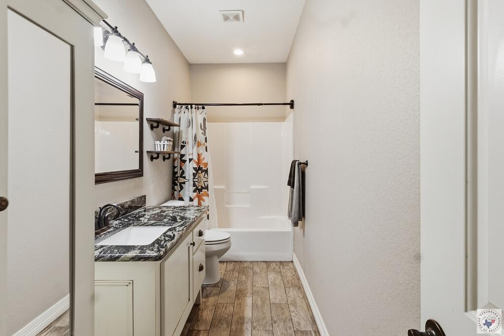 Bathroom with a dark marbled vanity countertop, patterned shower curtain, and wood-look flooring.