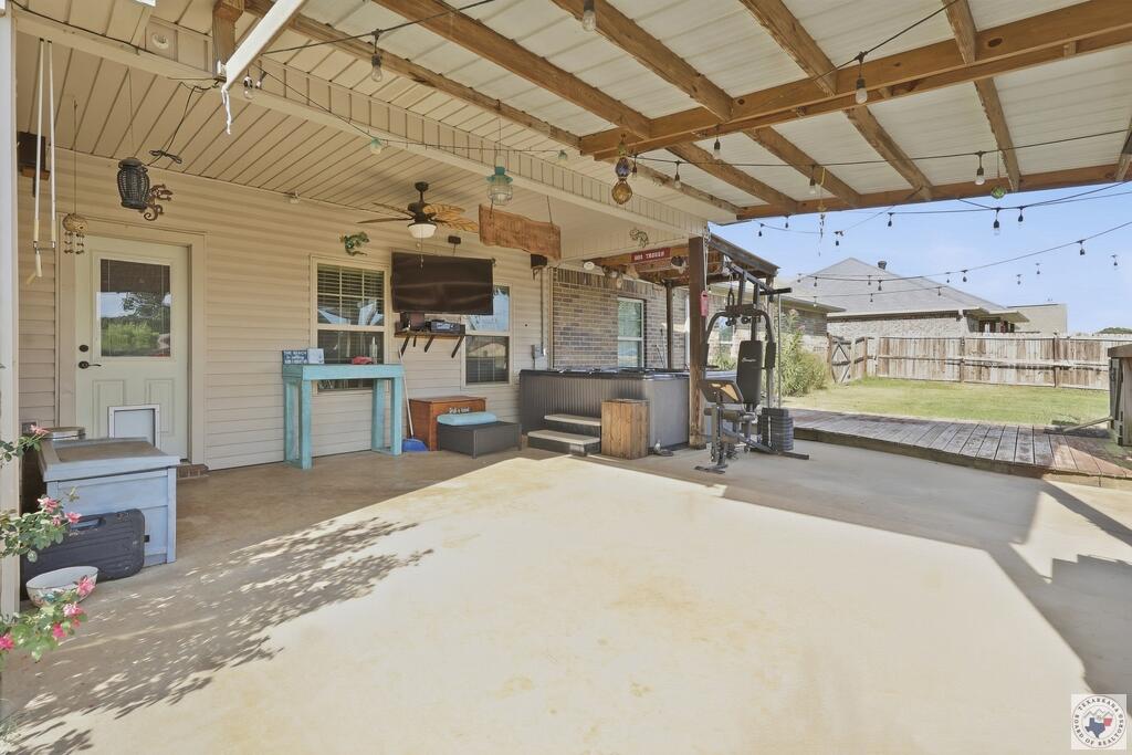 Covered patio with exposed beams, string lights, hot tub, and exercise equipment.