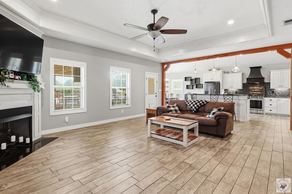 Open-plan living room and kitchen with a brown sofa, tiled floors, fireplace, and exposed wood beam.