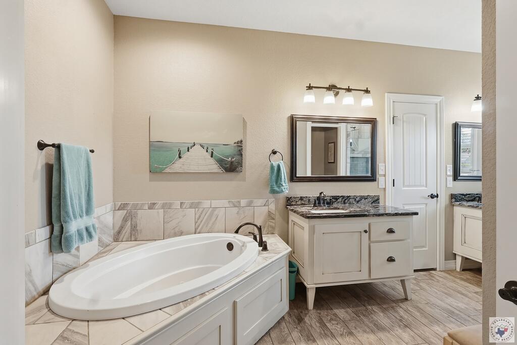 Bathroom with a built-in soaking tub, marble-look tile, and cream vanity with dark countertop.