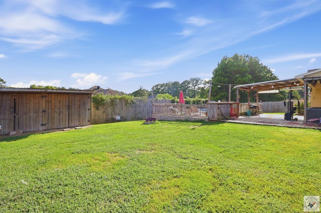 Fenced backyard with a broad lawn, wooden shed, raised deck, and covered patio.