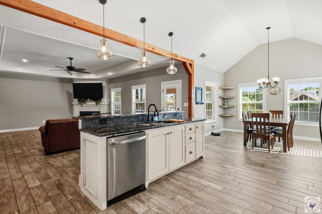 Open kitchen with a white island and dark backsplash adjoining a sunlit dining area.