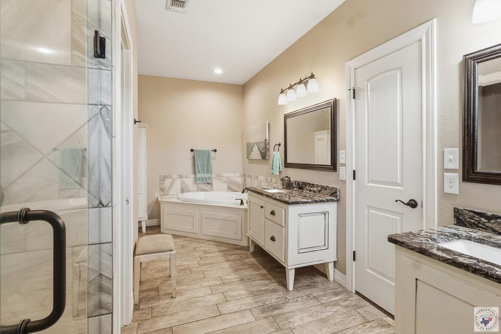 Bathroom with a glass shower, built-in soaking tub, and white granite-topped vanity.