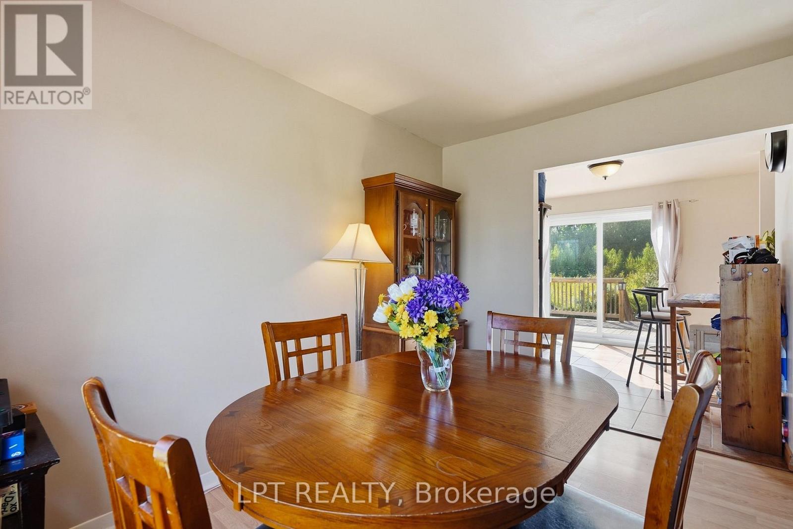 Dining room with an oval wooden table, flowers, and a bright adjoining room opening onto a deck.