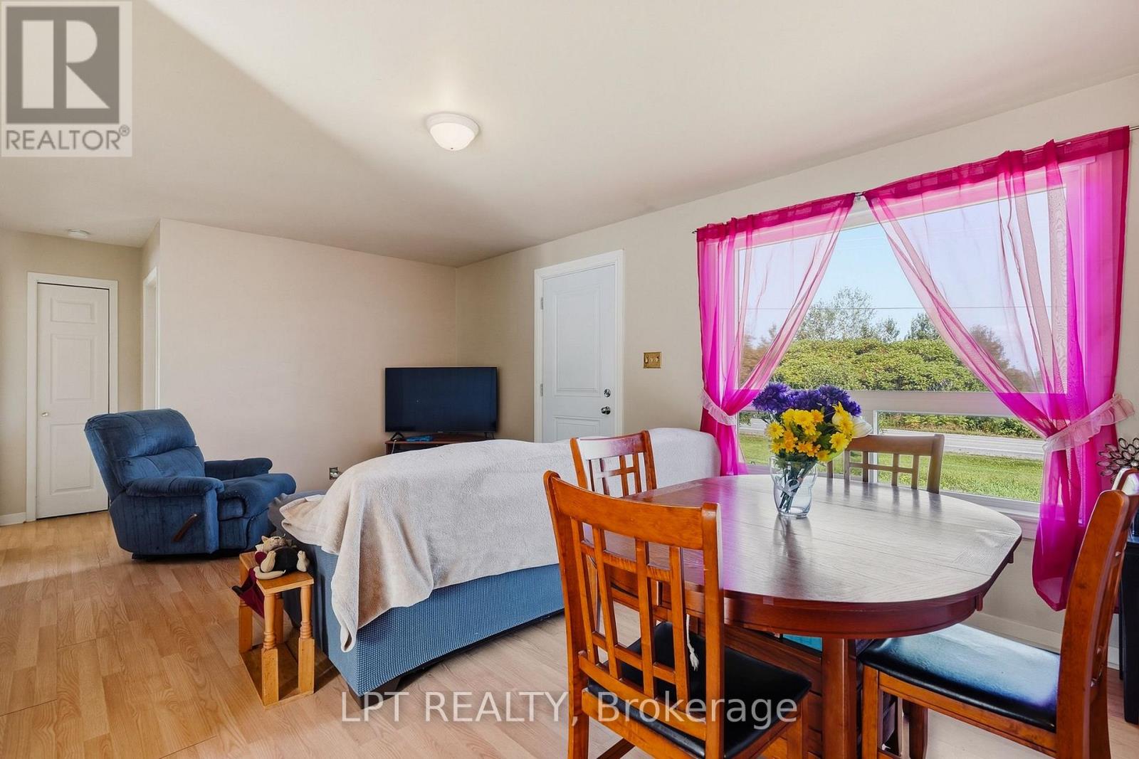 Furnished room with a dining table, covered bed, blue recliner, and bright pink curtains.