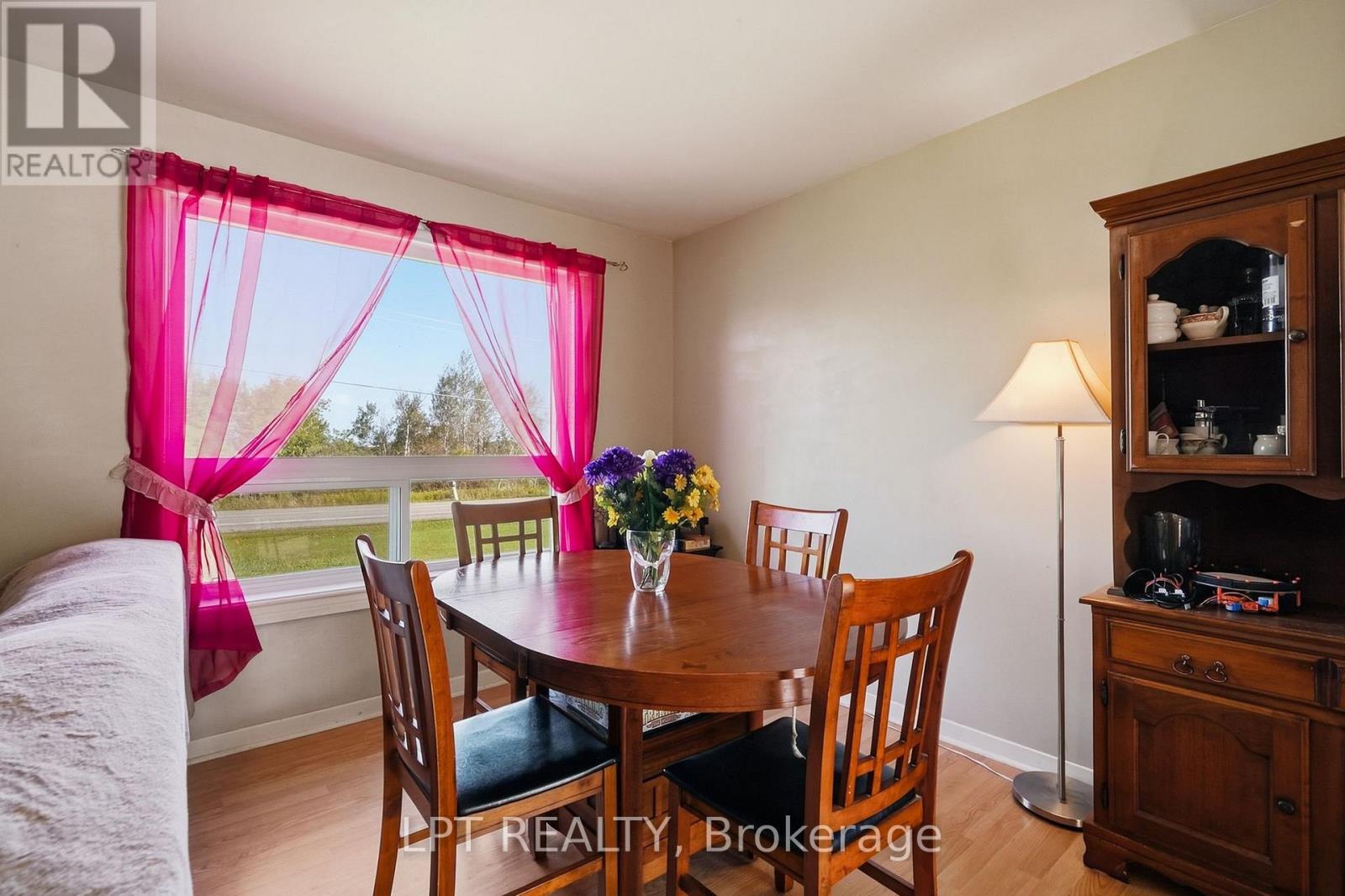 Dining room with a wooden table, china cabinet, and bright pink curtains around a large window.