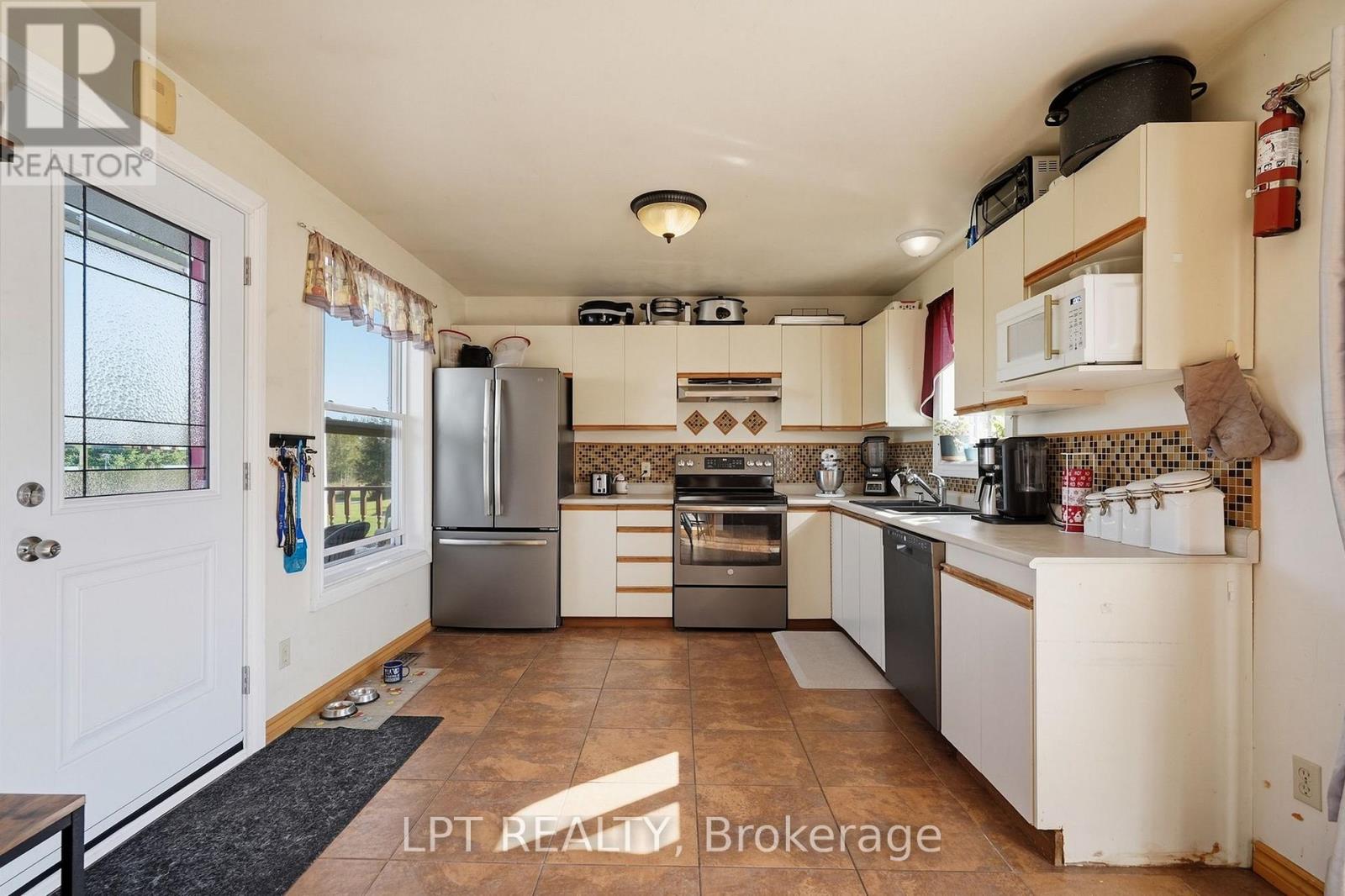 Kitchen with cream cabinets, stainless-steel appliances, mosaic backsplash, and brown tile floor.