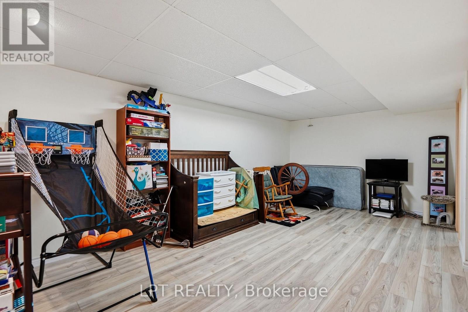 Furnished recreation room with a basketball arcade game, toy storage, and gray wood-look flooring.