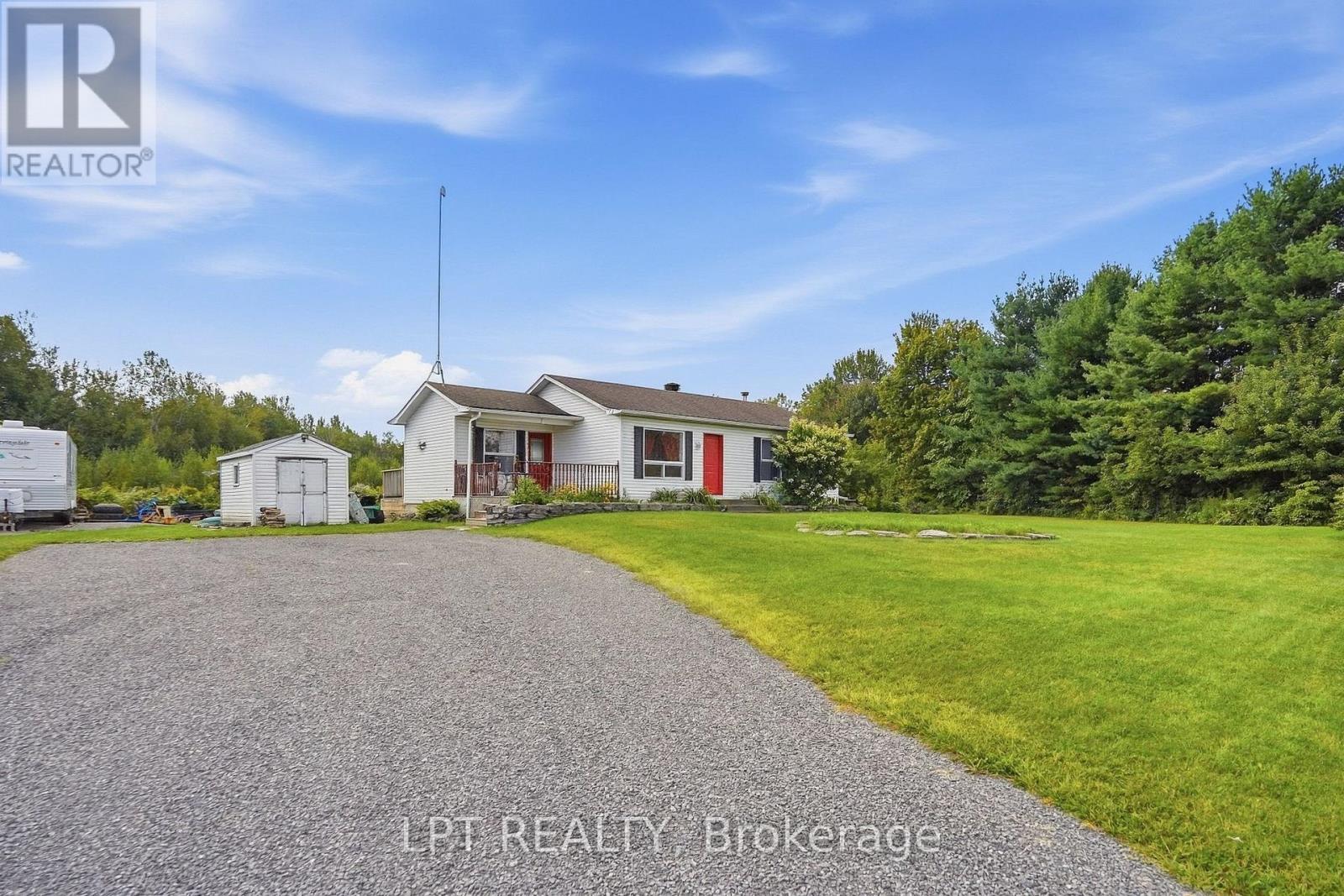 White bungalow with red doors beside a gravel drive and detached shed.