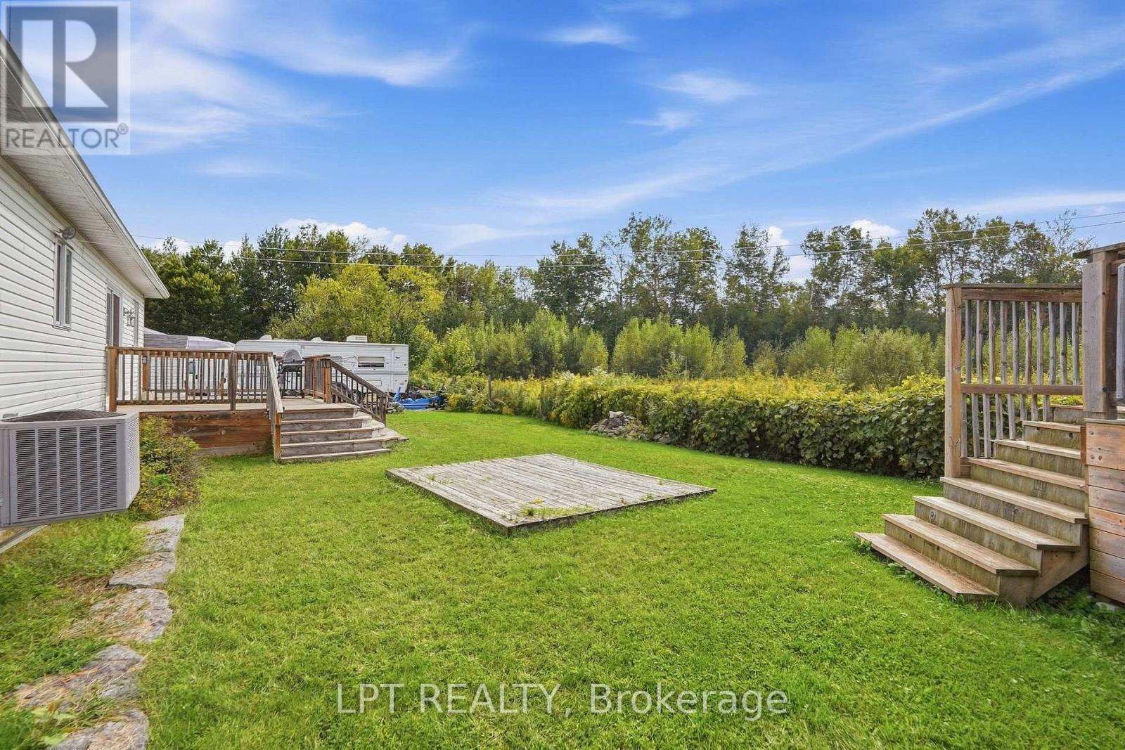 Backyard lawn with two wooden decks, a ground-level platform, hedge, and wooded tree line.