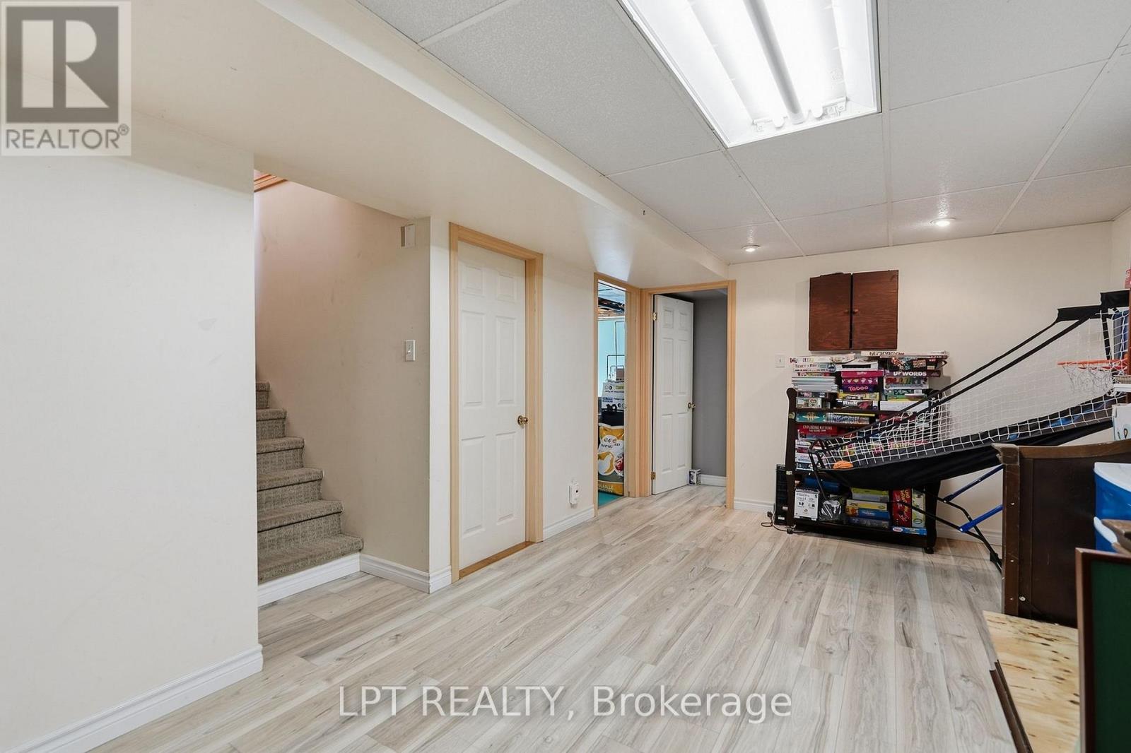 Finished basement recreation room with pale flooring, a carpeted staircase, and a stack of board games.