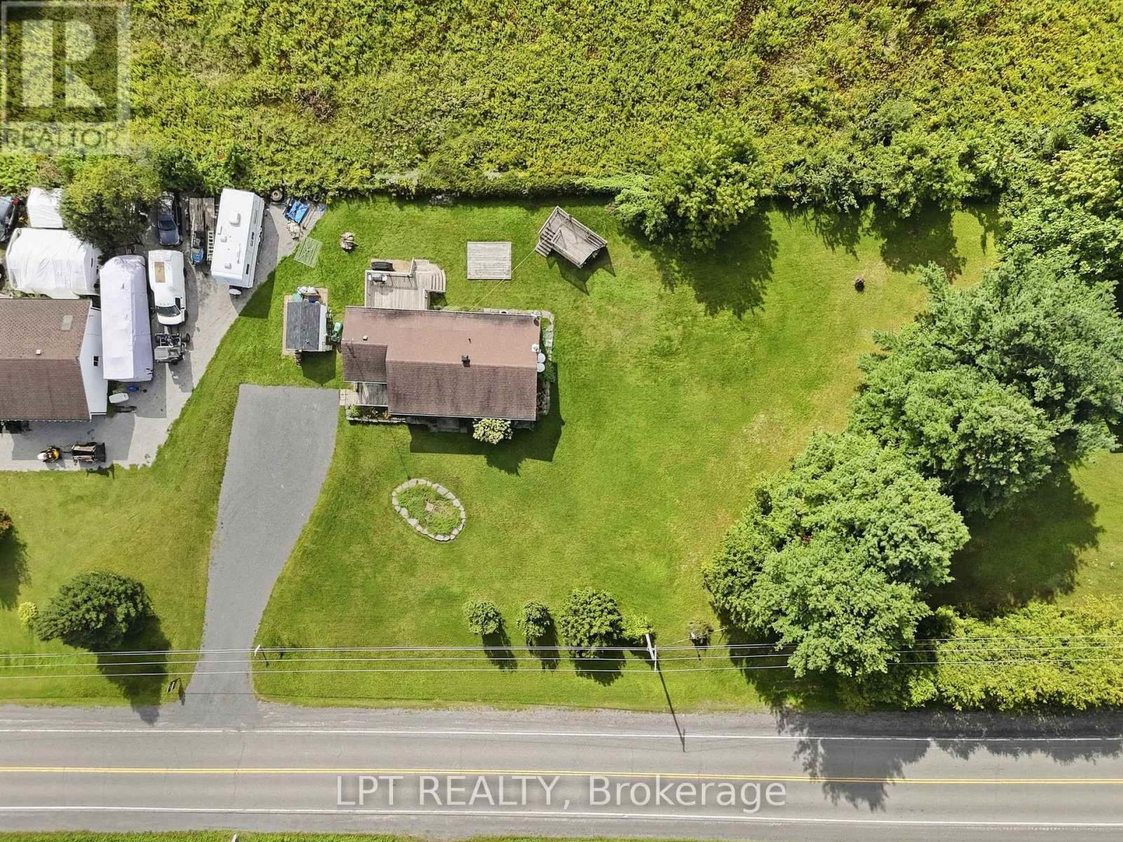 Aerial view of a home on a large lawn, with a long driveway, deck, gazebo, and mature trees.