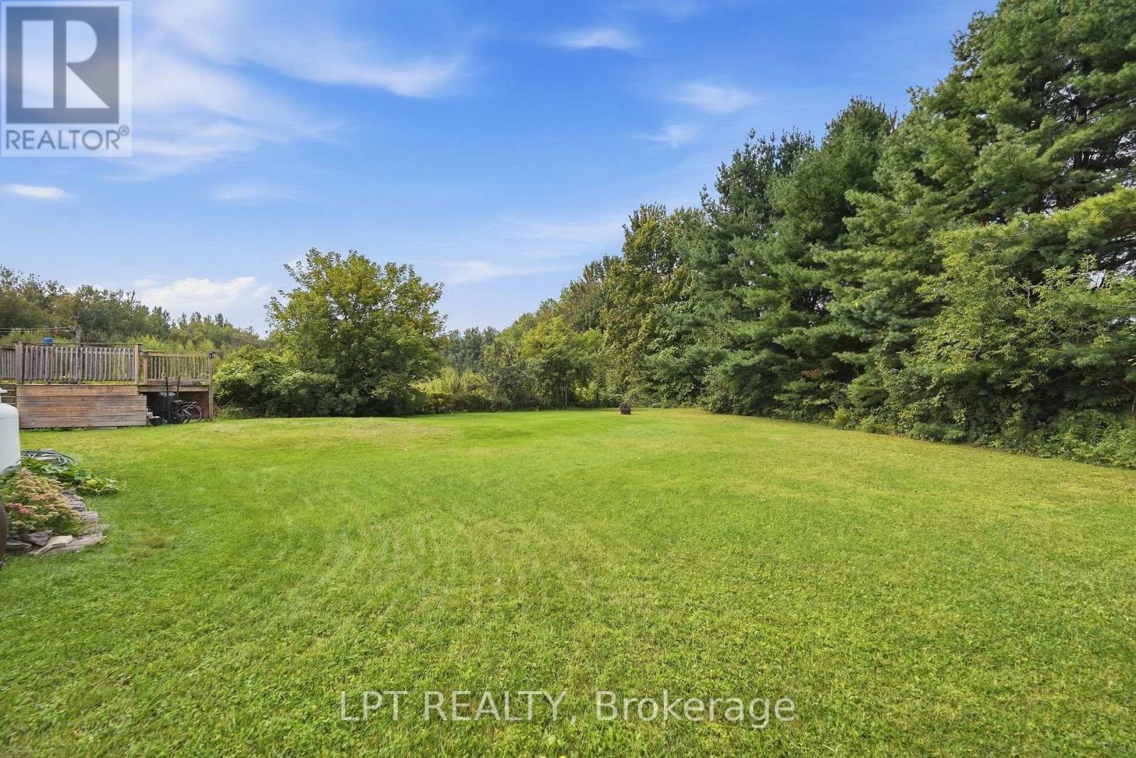 Spacious green backyard lawn bordered by mature trees, with a raised wooden deck.