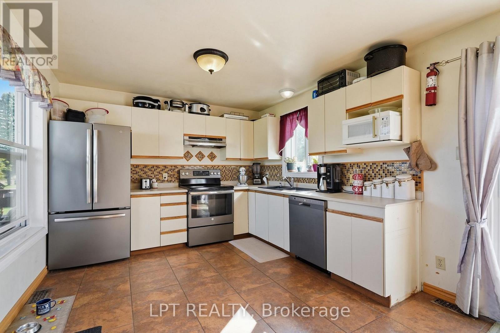 Kitchen with white wood-trimmed cabinets, stainless steel appliances, mosaic backsplash, and brown tile flooring.