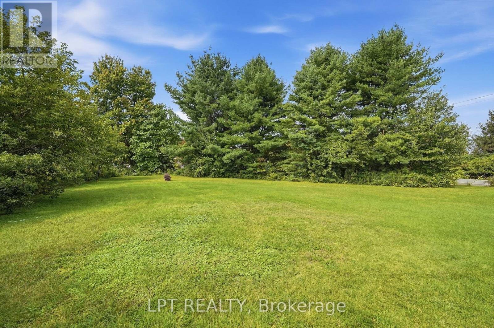 Expansive mown lawn bordered by mature trees and evergreens.