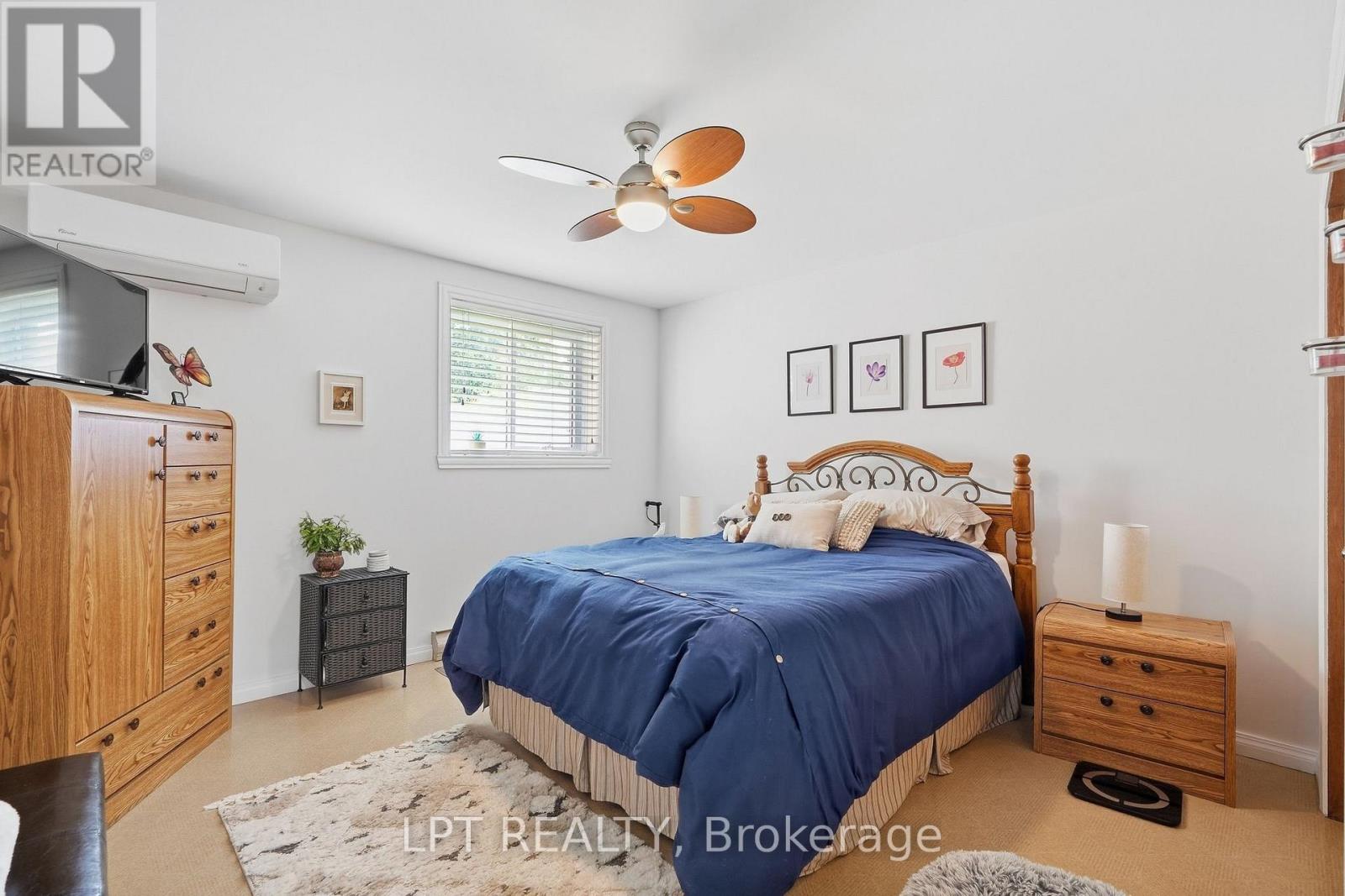 Furnished bedroom with a blue-covered bed, wooden dressers, and a ceiling fan.
